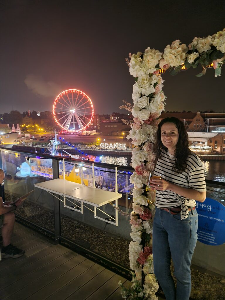 Woman standing on rooftop bar with cocktail in hand, beside floral arch