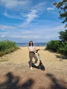 Woman standing on electric scooter, in front of beach