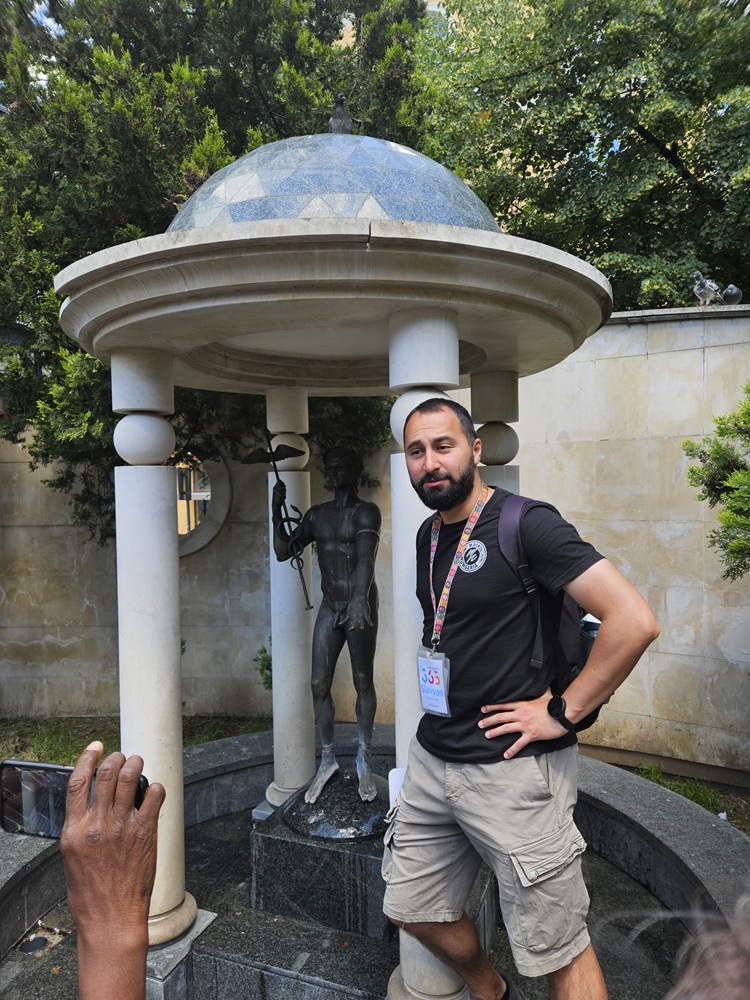 Male tour guide standing with hand on his hip in front of a water fountain